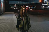 A woman is standing on a city sidewalk at night.