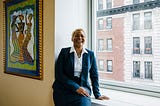 Rev. Dr. LaKeesha Walrond laughs while sitting on a window ledge in her fifth floor Upper Manhattan office.