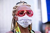 Black woman wearing a face mask that says “Show up for Black women.”