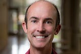 Head shot of Professor Ryan Hibbs smiling with background blurred.