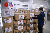 A worker arranges boxes of medical supplies, including 1,000 KN95 masks, 2,000 surgical masks, 100 protective suits and so on
