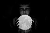 Black and white photo of a young boy holding a moon figure in his hands.