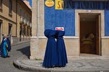 Two figures wearing blue robes stand together outside a building.