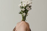A person with their head leaned all the way back holding a bunch of long-stemmed flowers in their mouth like a vase.