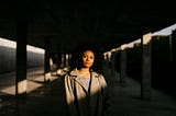 A Black woman standing in a dim parking garage with the light shining on her.