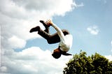 A Mormon missionary is captured against cloudy skies in a midair somersault, perhaps having bounced from a trampoline outside the frame.