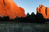 Red Rocks in Colorado Springs juts out of the ground as monoliths above the trees in the forefront.