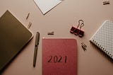 A few journals and stationary. The journal at the center is red and has “2021” inscribed on its cover.