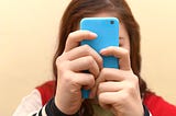 Close up of a teenager using her smartphone. Her face is obscured by her phone.