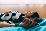 A young woman lies down and stares at the ceiling, holding her phone and feeling worried