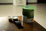 A single serve cup of yogurt next to a wristwatch.