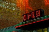 A photo of a neon OPEN sign on top of a business storefront.