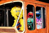 Sesame Street characters Big Bird, Elmo, Cookie Monster, and Abby Cadabby inside a bus.