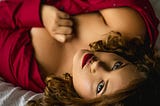 Photograph of woman in red reclining on bed, sensual feeling.