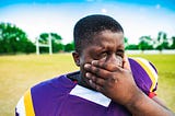 A close-up of a young football player rubbing his face with his hand in exhaustion.