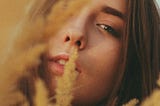 Calm young woman looking at camera through tall reeds in nature.