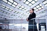 A woman wearing a long coat is standing in an airport terminal.