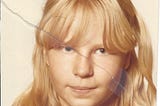 Picture of a 13-year old girl, long blond hair, bangs in her eyes, a wry smile. The picture ripped apart and taped together. It has faded colors.