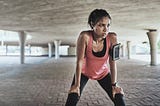 A sweaty young woman takes a break while exercising outdoors.