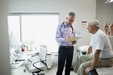 A doctor reviews the medical chart of a senior male patient.