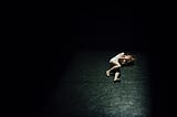 Distraught woman covering her face while lying on the ground against a black background.