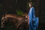 Boy sitting on brown horse beside wearing blue cloak