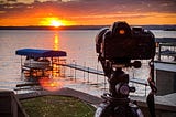 A camera on a tripod, looking at the rising sun over a lake