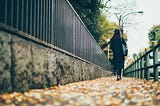 Woman walking down a leaf-strewn path.