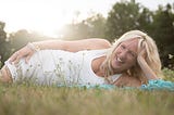 Liz Porter laying on her side in the grass in a white sleeveless dress laughing
