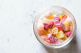 Jar of colourful gummy candies on a white marble background.