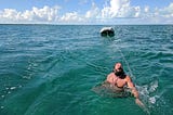 The author being towed behind a sailboat in turquoise, Bahamas water