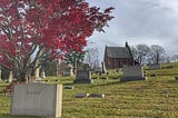 A brick chapel beside a red-leafed tree in a cemetary.