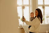 Mother holding baby son and taking a photo of something.