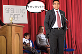 A man in a grey business suit stands confidently at a microphone on a red-curtained stage, a speech bubble above him spelling “B-O-U-Q-U-E-T!!” Behind him, two young children sit looking unimpressed beside a woman at a wooden podium, a small gold trophy, and a handmade “Spelling Bee” sign.