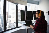 photo of a programmer with multiple screens looking out of an apartment window