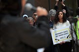 Focus is on a woman holding a “immigrant’s rights are human rights” sign.