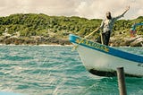 Nipsey Hussle on a boat with his left hand raised. A still from his music video for “Victory Lap”