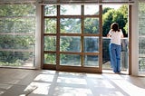 View through an empty room of a woman standing on a balcony.