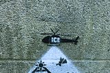 A concrete wall with a painting depicting an ICE helicopter flying above a nativity scene.