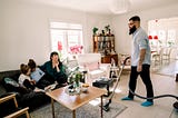 Man looking at family while cleaning carpet with vacuum cleaner in living room