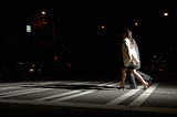 Side view of a young man and woman crossing the street at night.