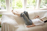 Woman sleeping on sofa in living room, book covering face.