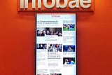 A computer monitor displays the homepage of infobae.com, an Argentine news website. The wall behind it is bright orange.