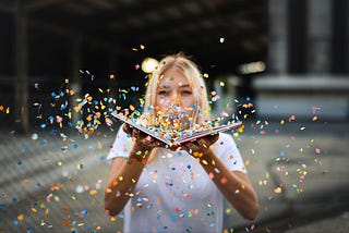 A woman blows confetti from a book
