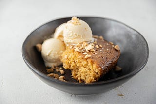 Image shows a piece of cake in a bowl with two scoops of ice cream next to it.