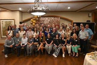 A whole lot of old people gather in a banquet room for a group photo.