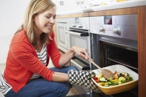Woman putting tray of roast vegetables in oven