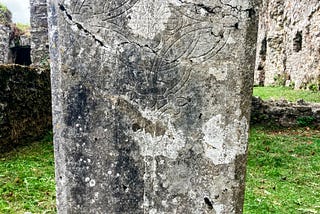 A gravestone with a Celtic cross, grey and lichen covered stone against the green mown grass. Bridgestone Priory. Cork. Ireland.