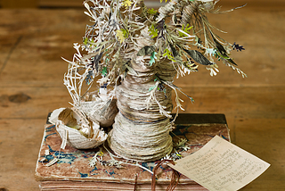 a tree that is crafted out of the pages of a book, shown in a photograph on top of an older book