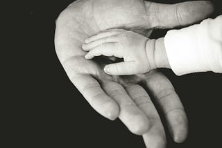 A child’s small hand rests in an adult’s larger hand.
